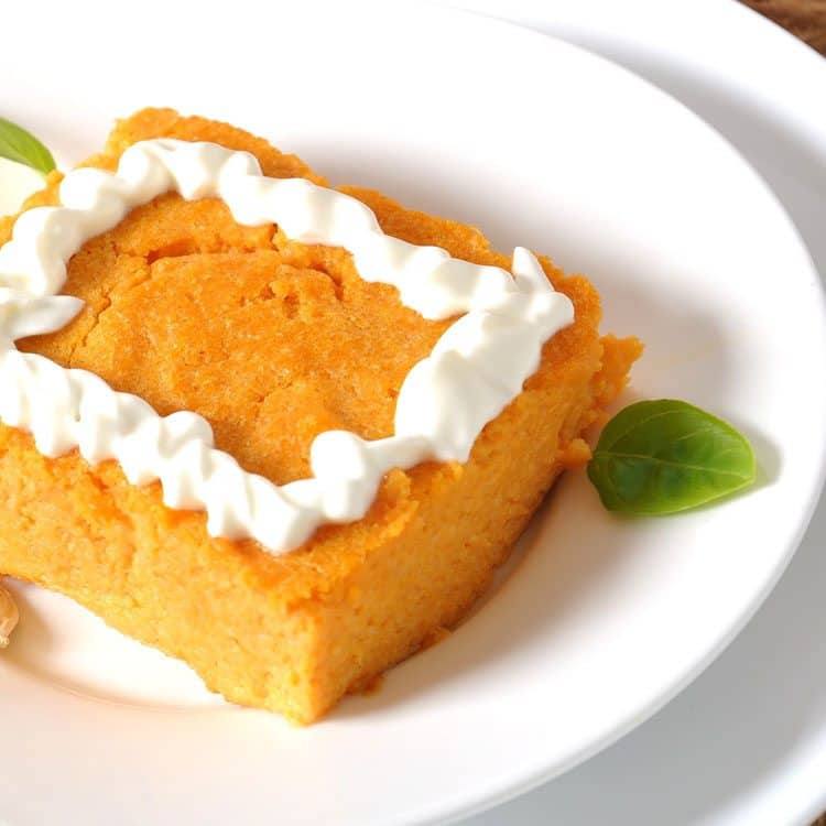 Close-up of a square slice of crustless pumpkin pie with whipped topping and a basil leaf