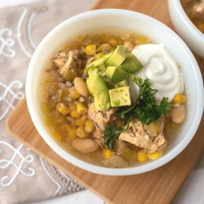 Slow cooker white chicken chili in a white bowl topped with avocado, sour cream, and fresh herbs