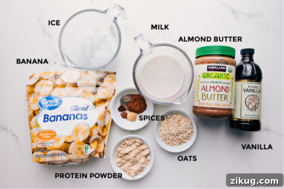 All the fresh ingredients laid out for making the best chai smoothie recipe, including milk, frozen banana slices, vanilla extract, cinnamon, cardamom, ginger, nutmeg, cloves, salt, old-fashioned oats, almond butter, vanilla protein powder, and ice cubes.