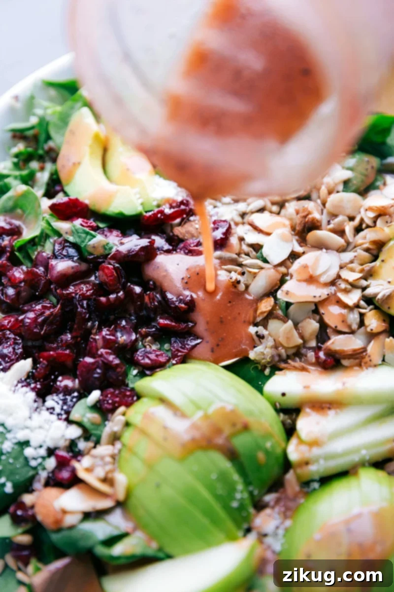 Fresh raspberry vinaigrette being drizzled generously over the mixed Quinoa and Almond Salad ingredients.