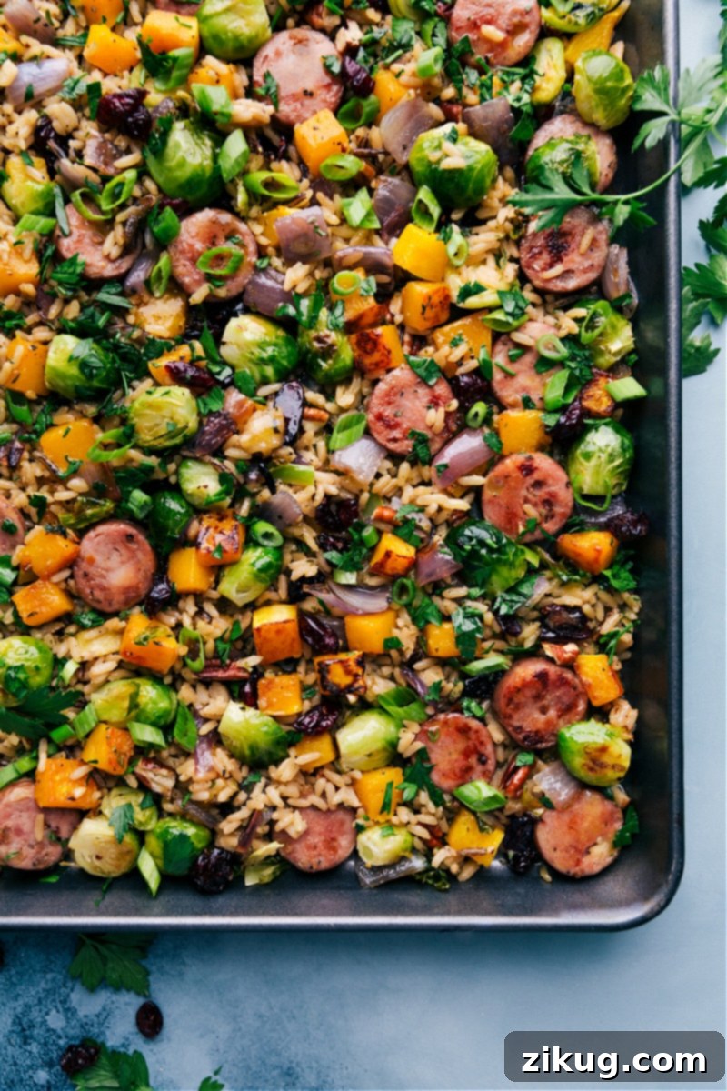 Butternut Squash Wild Rice Pilaf: A delicious and unique ONE-PAN meal with roasted wild rice, smoked chicken & apple sausage, maple butternut squash, and caramelized Brussels sprouts, drizzled in an irresistible maple-orange vinaigrette. Even the wild rice cooks on the sheet pan! Overhead view of Butternut Squash Wild Rice Pilaf in a large sheet pan, showcasing roasted vegetables, sausage, and wild rice