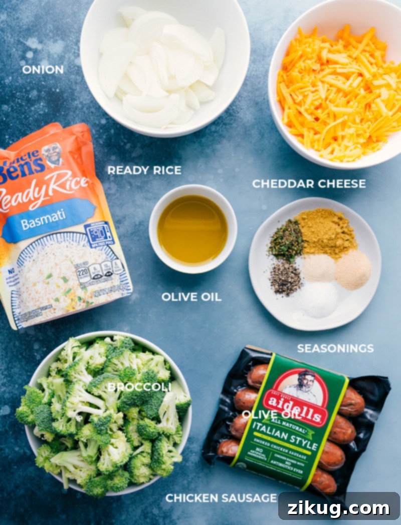 Key Ingredients for Easy Cheesy Chicken, Broccoli, and Rice All the fresh and pre-packaged ingredients for Cheesy Chicken, Broccoli, and Rice laid out on a white kitchen counter, showcasing chopped broccoli florets, thinly sliced yellow onion, smoked chicken sausage, microwaveable Ready Rice packets, olive oil, and various seasoning jars.