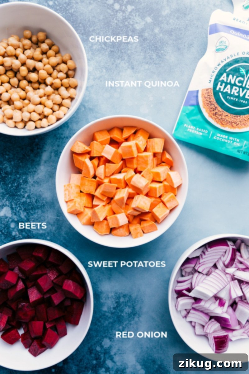 A vibrant display of fresh ingredients for Sheet Pan Quinoa Pilaf, including sweet potatoes, beets, red onion, chickpeas, and clementines.