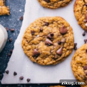 A stack of three golden-brown Pumpkin Oatmeal Chocolate Chip Cookies, with visible oats and melted chocolate chips, resting on a white surface.