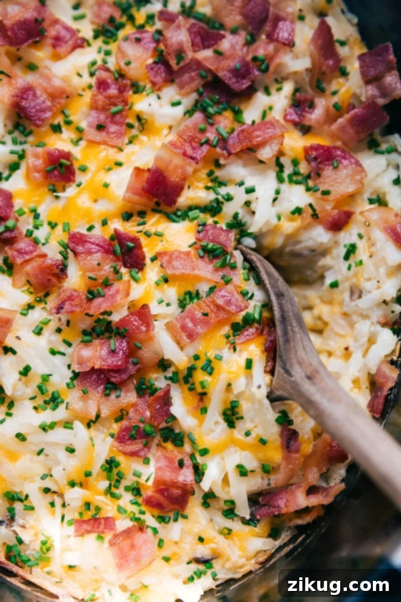Comfort in a Spoon: Ready-to-Serve Hearty Crockpot Hashbrown Casserole A warm, hearty scoop of crockpot hashbrown casserole, steaming and ready to be served, garnished with fresh chives and crispy bacon.