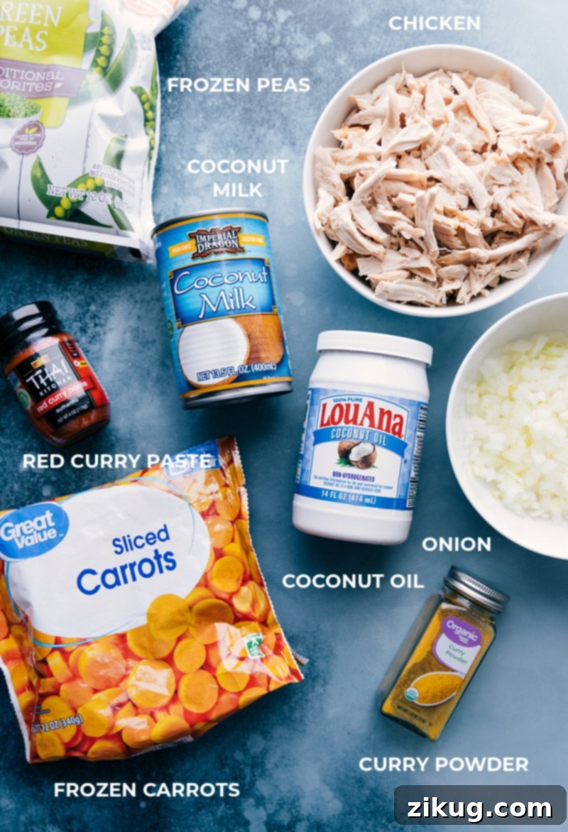 All the essential ingredients for Quick Chicken Curry, including frozen peas, a can of full-fat coconut milk, shredded rotisserie chicken, red curry paste, coconut oil, diced onions, pre-sliced carrots, and various seasonings, neatly prepped and laid out for easy assembly.