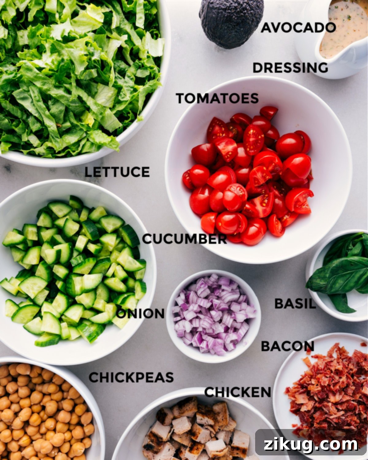 Ingredients In Chopped Chicken Salad This recipe has everything prepped for easy assembly: tomatoes, avocado, dressing, lettuce, cucumbers, onions, basil, bacon, chicken, and chickpeas.