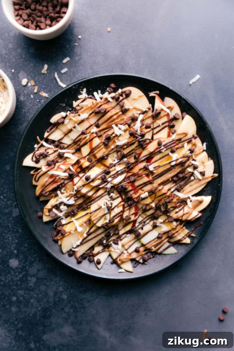 Indulgent Apple Nachos: A decadent dessert with chocolate drizzle and sweet toppings. Easy to make and a guaranteed crowd-pleaser! #applenachos #dessert #chocolate #fruitdessert #sweettooth Overhead image of the chocolate version of this treat, featuring apple slices drizzled with melted chocolate and other sweet dessert toppings.