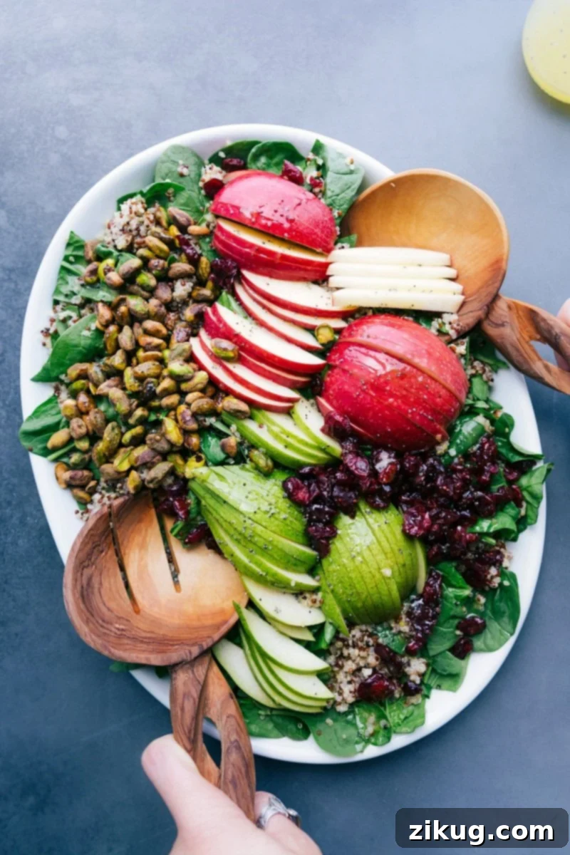 Quinoa apple salad on a platter with fresh greens, sliced apples, nuts, and more.