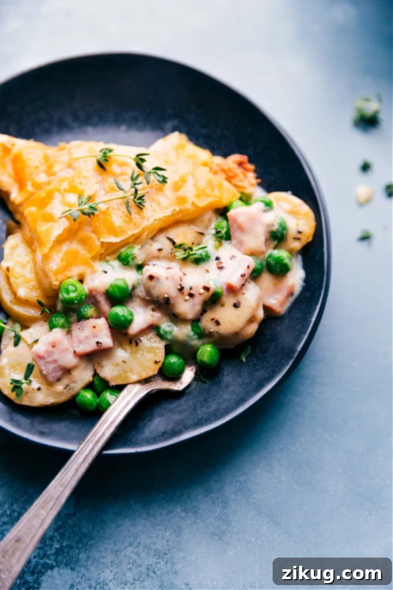A generous slice of Ham and Potato Pot Pie on a plate, showcasing the creamy filling and golden puff pastry.