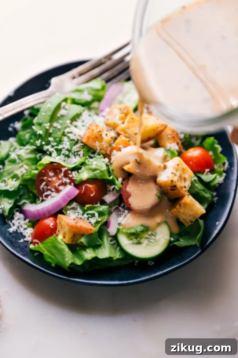 Herbed Italian Vinaigrette 3 Homemade Italian dressing being poured generously over a vibrant, colorful garden salad with mixed greens and fresh vegetables.