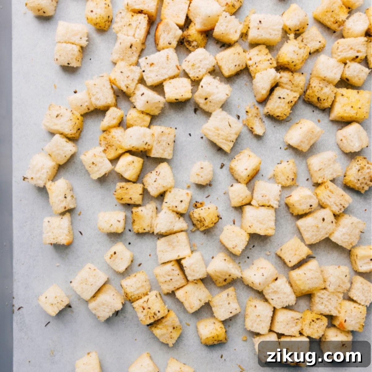 Homemade croutons spread in an even layer on a sheet pan, perfectly coated in olive oil and seasonings, ready for roasting in the oven.