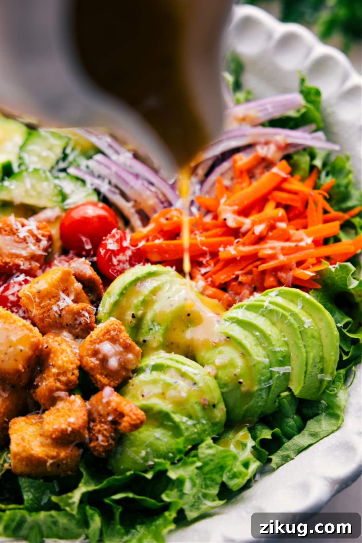 The finished garden salad, beautifully presented in a large bowl, is being drizzled with homemade vinaigrette, ready to be tossed and served.