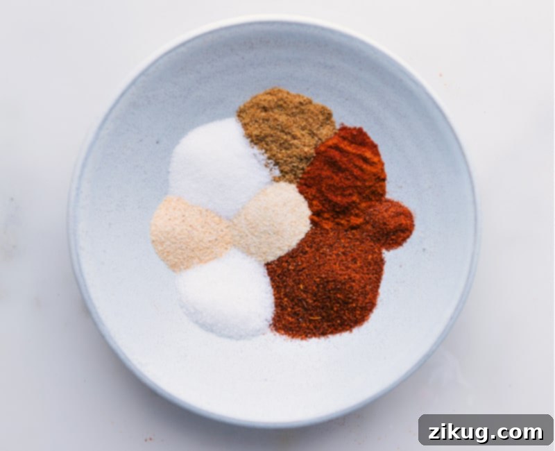 Our favorite Fajita Seasoning blend is incredibly simple to make, utilizing common spices you likely already have in your pantry! Bypass the store-bought packets; you'll never want to revert once you experience the ease and superior taste of preparing your own seasoning blends. This recipe elevates your chicken fajitas to a new level of deliciousness. #homemade #mexican #fajita #seasoning #mix #chickenfajitas #easyrecipe Overhead image of all the individual spices added to a mixing bowl, ready to be combined