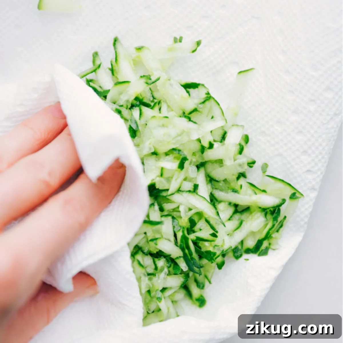 The Crucial Step: Squeezing Cucumber for the Perfect Tzatziki Texture Hands firmly pressing a ball of grated cucumber enclosed in a clean kitchen towel, vigorously extracting excess liquid to ensure a perfectly thick and creamy Tzatziki Sauce.