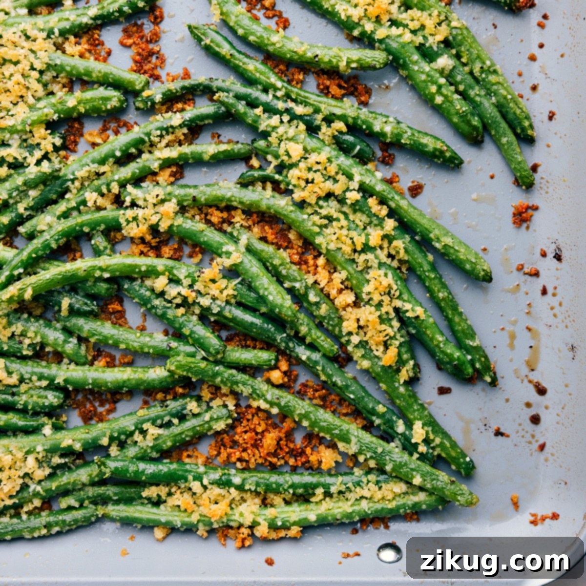 Easy And Delicious Roasted Green Beans Made Two Different Ways Two variations of roasted green beans on a tray: one simple seasoned, the other with a crispy panko and parmesan coating.