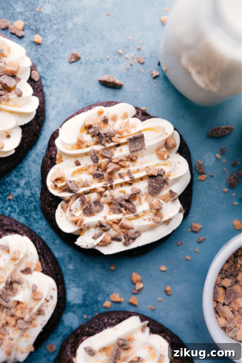 The best ever Heath Bar Cookies! Inspired by 'Better Than Anything' cakes, these ultimate cookies are gooey, caramel-loaded, piled high with whipped cream frosting, and garnished with crushed toffee bits. Recipe via ChelseasMessyApron #dessert #best #quick #easy #simple #frosting #candybar #caramel #heathbar #cookies Up-close, overhead view of beautifully frosted and toffee-topped Heath Bar Cookies, showcasing their irresistible texture