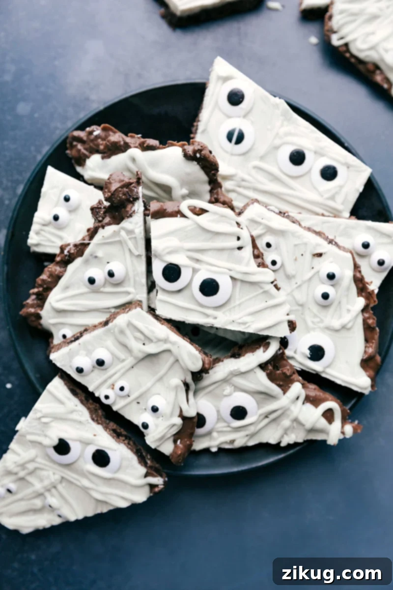 A plate displaying a beautifully crafted Mummy Bark, a cute and delicious festive treat, perfect for Halloween gatherings or other special occasions. The bark features white chocolate 'bandages' and whimsical candy eyes over a dark chocolate and Oreo base.