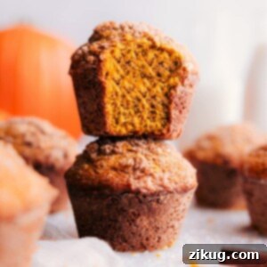 Irresistible Pumpkin Muffins 3 A stack of perfectly baked pumpkin muffins with a warm, golden tone, one at the front displaying a bite taken, revealing the moist, spiced interior and inviting texture.