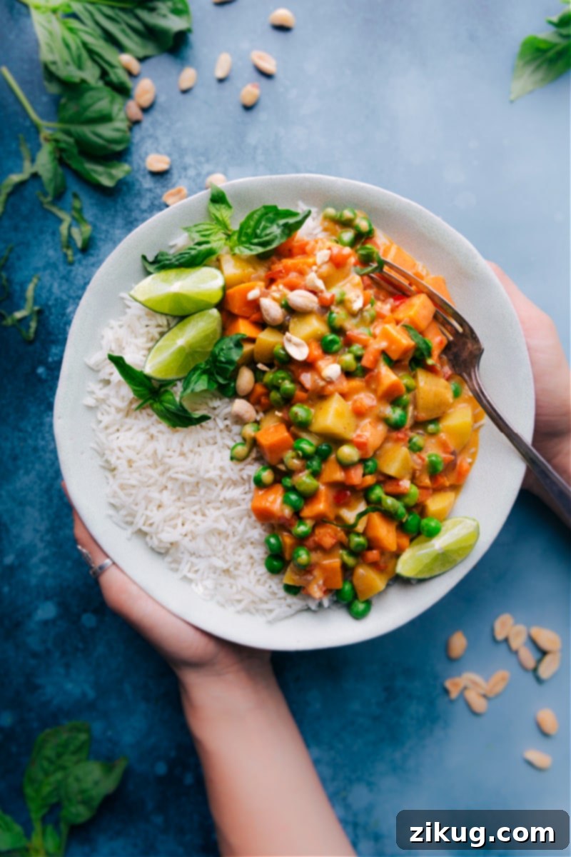 Delicious Panang Curry with sweet and golden potatoes in a rich coconut sauce, garnished with basil and peanuts. Overhead image of Panang Curry in a bowl, generously garnished with fresh basil leaves, crunchy crushed peanuts, and bright lime wedges. The curry is rich and creamy with visible vegetables and potatoes.