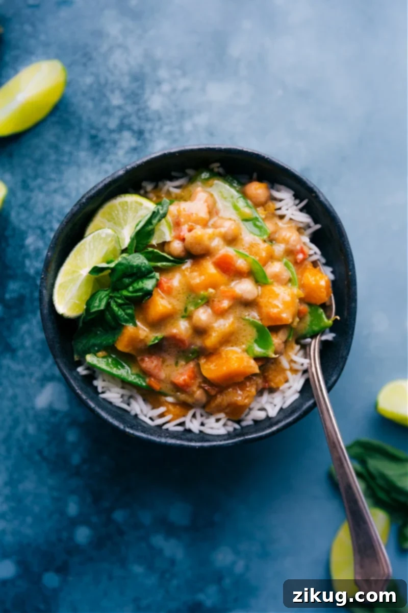 Vegetarian Thai Green Curry combines a medley of aromatic veggies with a vibrant green curry paste, tender butternut squash, and crisp snow peas in a creamy, indulgent coconut base. Top your bowl with fresh lime and basil for a meal you won't be able to get enough of! Recipe via ChelseasMessyApron #dinner #quick #easy #simple #best #rice #chickpeas #beans #healthy #whole #wholefoods #vegetarian #thai #green #curry Overhead image of Vegetarian Thai Green Curry, garnished with fresh lime and basil