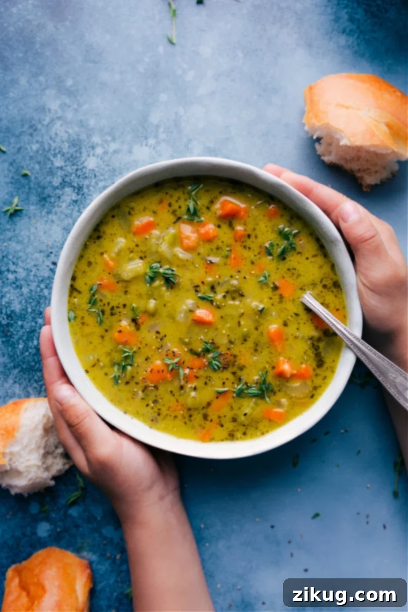 Overhead image of a steaming bowl of vegetarian split pea soup, garnished with fresh herbs and a slice of crusty bread on the side.