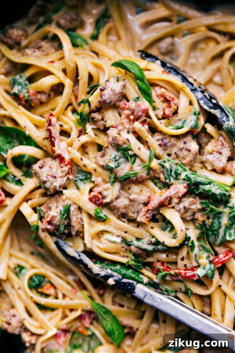 Creamy Sausage Pasta: A 30-Minute Recipe for Weeknight Indulgence Overhead image of a generous serving of Creamy Sausage Pasta in a large pot, showcasing thick fettuccine, crumbled Italian sausage, vibrant sun-dried tomatoes, and wilted spinach, all coated in a rich, creamy sauce.