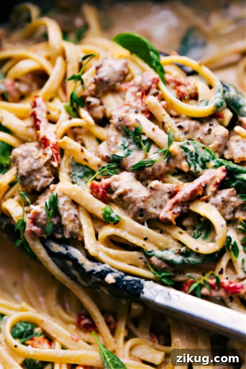 Delicious Creamy Sausage Pasta ready to be served from the pot. Up-close overhead shot of Creamy Sausage Pasta served directly in the pot, highlighting the creamy sauce, tender fettuccine, crumbles of sausage, and bright spinach and sun-dried tomatoes.