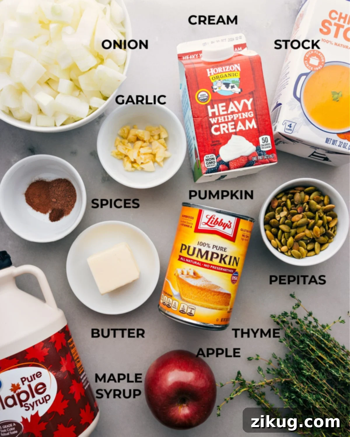 A vibrant display of all the essential ingredients for pumpkin soup, meticulously prepped and arranged for easy assembly. This includes diced sweet onions, minced garlic cloves, a can of rich pumpkin puree, a crisp Fuji apple, aromatic spices like cinnamon, nutmeg, and cloves, fresh thyme, pure maple syrup, hearty chicken stock, creamy heavy cream, and a scattering of crunchy pepitas for garnish.