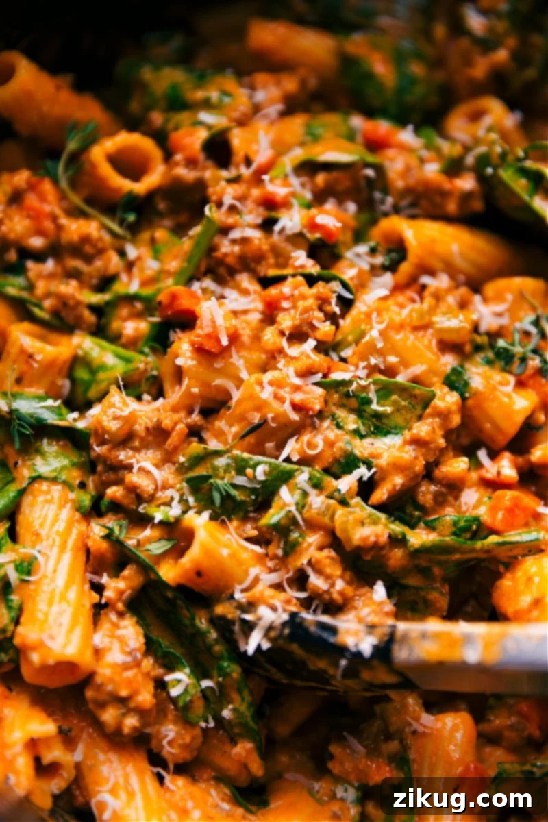 This robust Sausage Rigatoni recipe is made with everyday ingredients and ready in about 30 minutes. Perfectly cooked rigatoni is tossed in a luxuriously rich sauce with tender spinach and Italian-seasoned sausage. It's a quick, easy, simple, best pasta dish, perfect for family-friendly, kid-friendly dinners made on the stove. #dinner #quick #easy #simple #best #pasta #stove #familyfriendly #spinach #kidfriendly #sausage #rigatoni Overhead image of Creamy Sausage Rigatoni in a pot, garnished with fresh herbs and Parmesan cheese