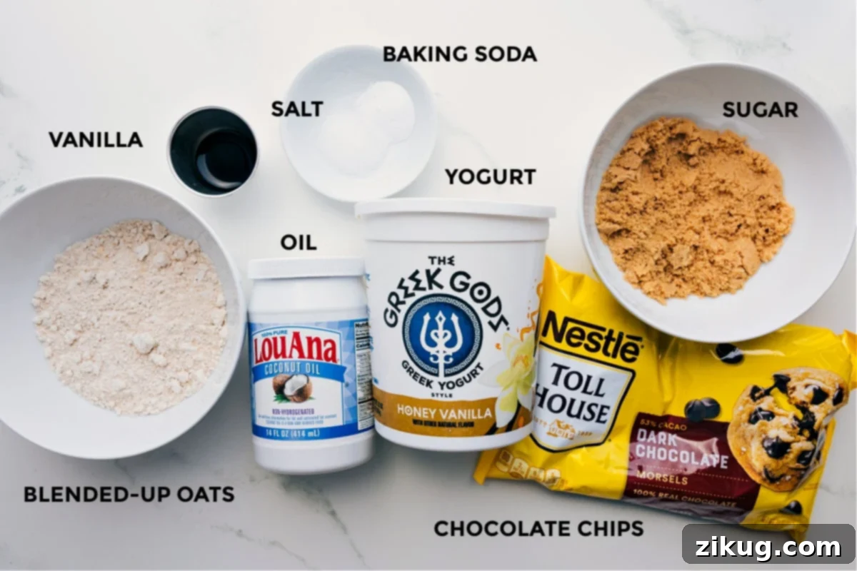 Carefully prepped ingredients laid out for making healthy brownies, including blended oats for flour, vanilla, salt, baking soda, coconut oil, Greek yogurt, dark chocolate chips, and coconut sugar.