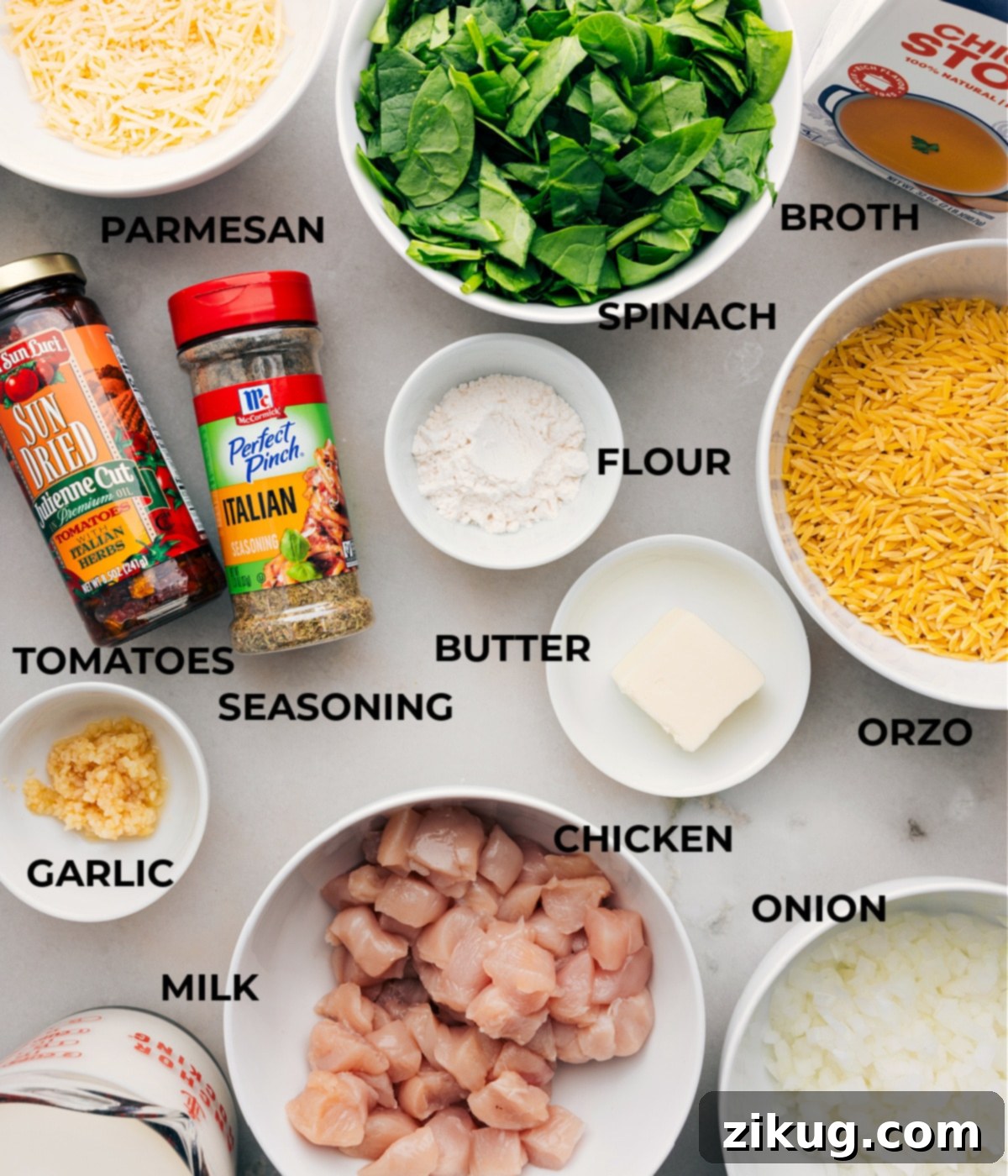Essential Ingredients For Creamy One-Pot Chicken Orzo Recipe All the ingredients for the creamy one-pot chicken orzo recipe are neatly prepped on a counter, including fresh spinach, chicken broth, diced vegetables, orzo pasta, chicken pieces, various seasonings, grated cheese, and a bottle of milk, ready for assembly.