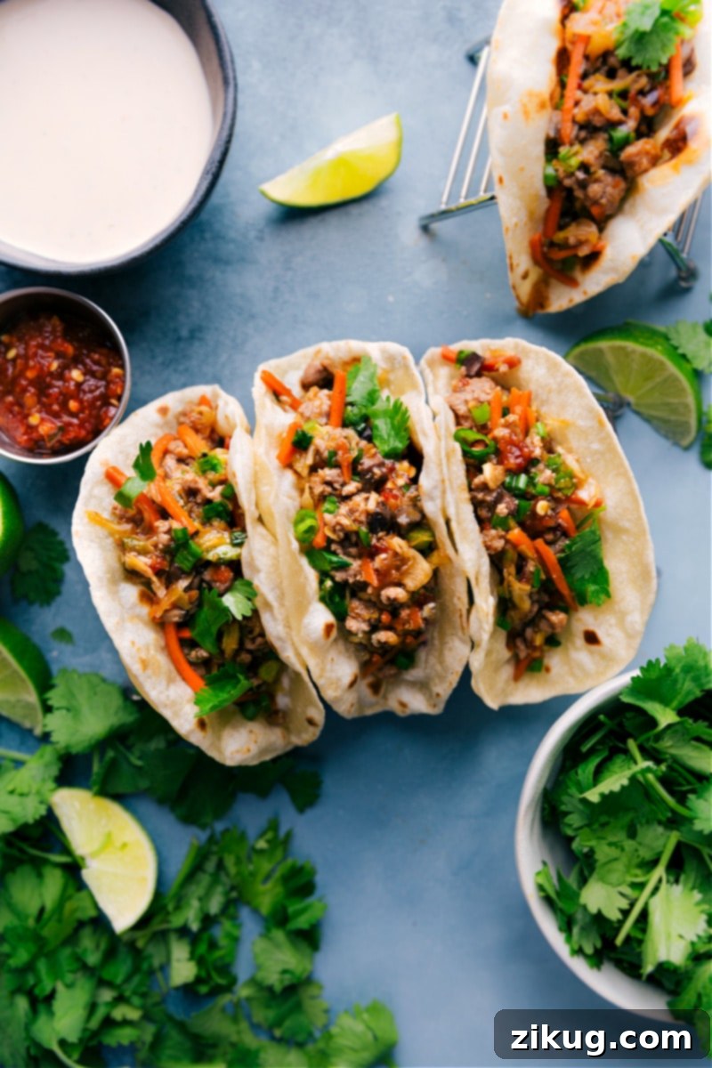 Delicious Asian Pork Tacos with spicy mayo and fresh cilantro. Overhead shot of two fully assembled Asian Pork Tacos on a white plate, garnished with fresh cilantro and lime wedges.