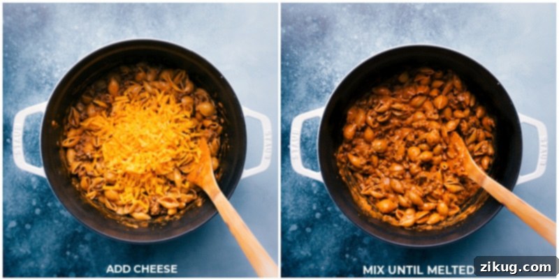 The final, irresistible touch: Melting sharp cheddar cheese into the creamy beef and shell pasta, creating a perfectly blended, luxurious, and utterly comforting dish ready to be served. Process shots: Adding freshly shredded sharp Cheddar cheese to the Creamy Beef and Shells and gently stirring until it melts into a rich, gooey sauce.