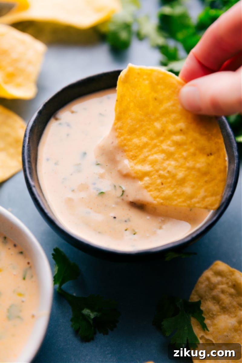 Experience the ultimate Creamy Queso Dip: ridiculously cheesy, perfectly seasoned, and ideal for dipping your favorite salted tortilla chips. This quick and easy stovetop recipe will be your new go-to appetizer for game day or any party! Overhead image of a chip being dipped into a bowl of golden, creamy Queso Dip, showcasing its rich, molten texture and inviting appeal. Perfect for an easy homemade cheese dip.