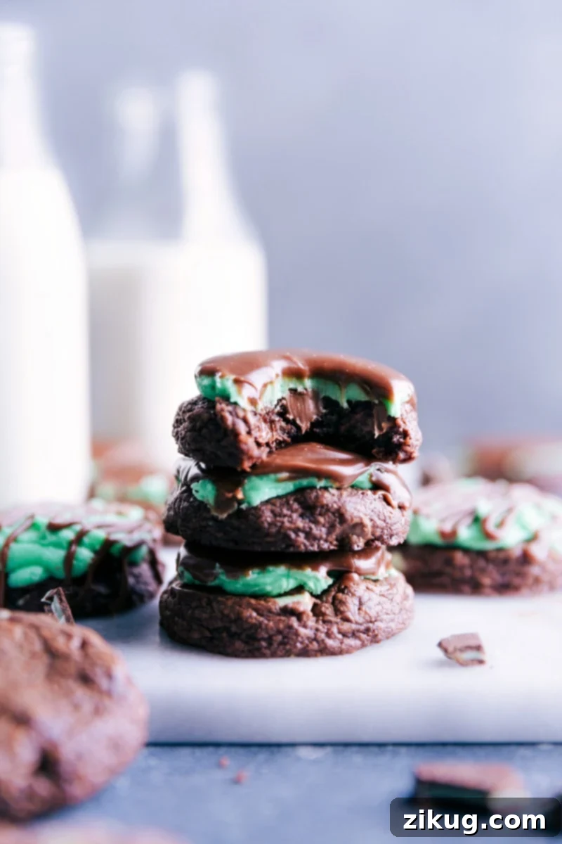 A beautiful stack of three Mint Brownie Cookies, with a bite taken out of the top one to reveal the dense chocolate cookie, creamy green peppermint frosting, and glossy dark chocolate ganache.