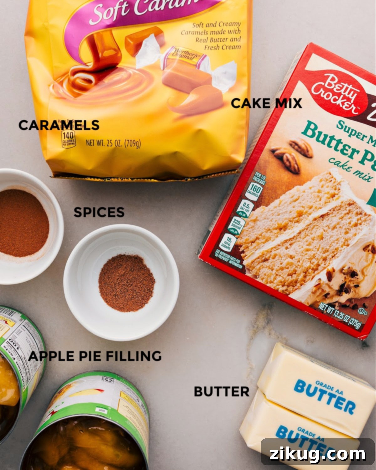 Apple Dump Cake Ingredients All the ingredients for this recipe are set out for easy assembly, including caramels, cake mix, spices, butter, and pie filling.