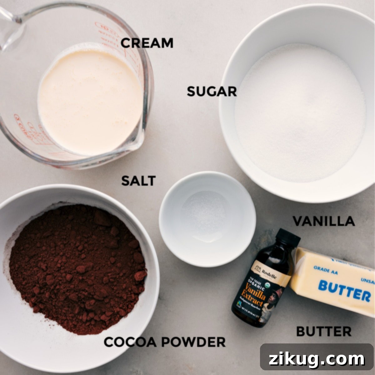 Essential ingredients for homemade hot fudge sauce are neatly arranged: sugar, salt, heavy cream, high-quality cocoa powder, vanilla extract, and unsalted butter.