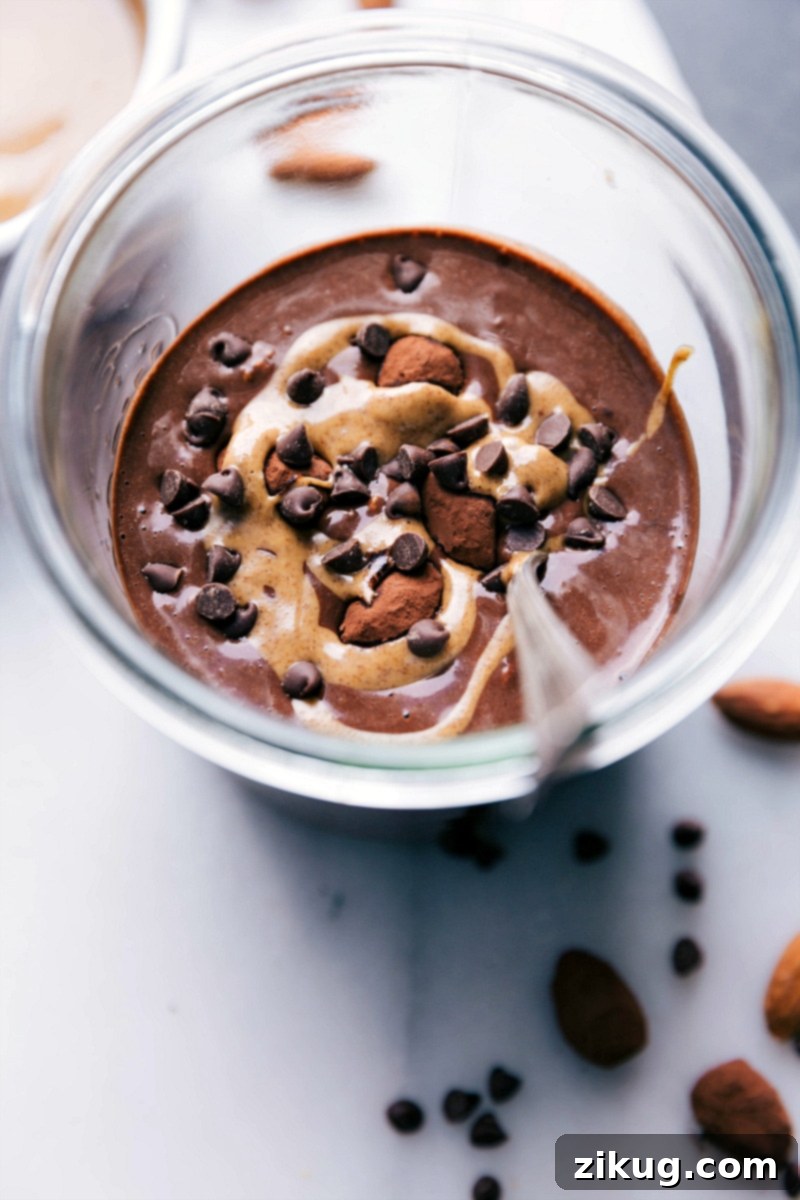 Indulgent Chocolate Almond Overnight Oats Topped with Swirled Almond Butter and Chips A vibrant and appetizing bowl of Chocolate Almond Overnight Oats, perfectly prepared with chocolate almond milk, adorned with a luscious swirl of creamy almond butter and a scattering of miniature chocolate chips, ready for a delightful and nourishing meal.