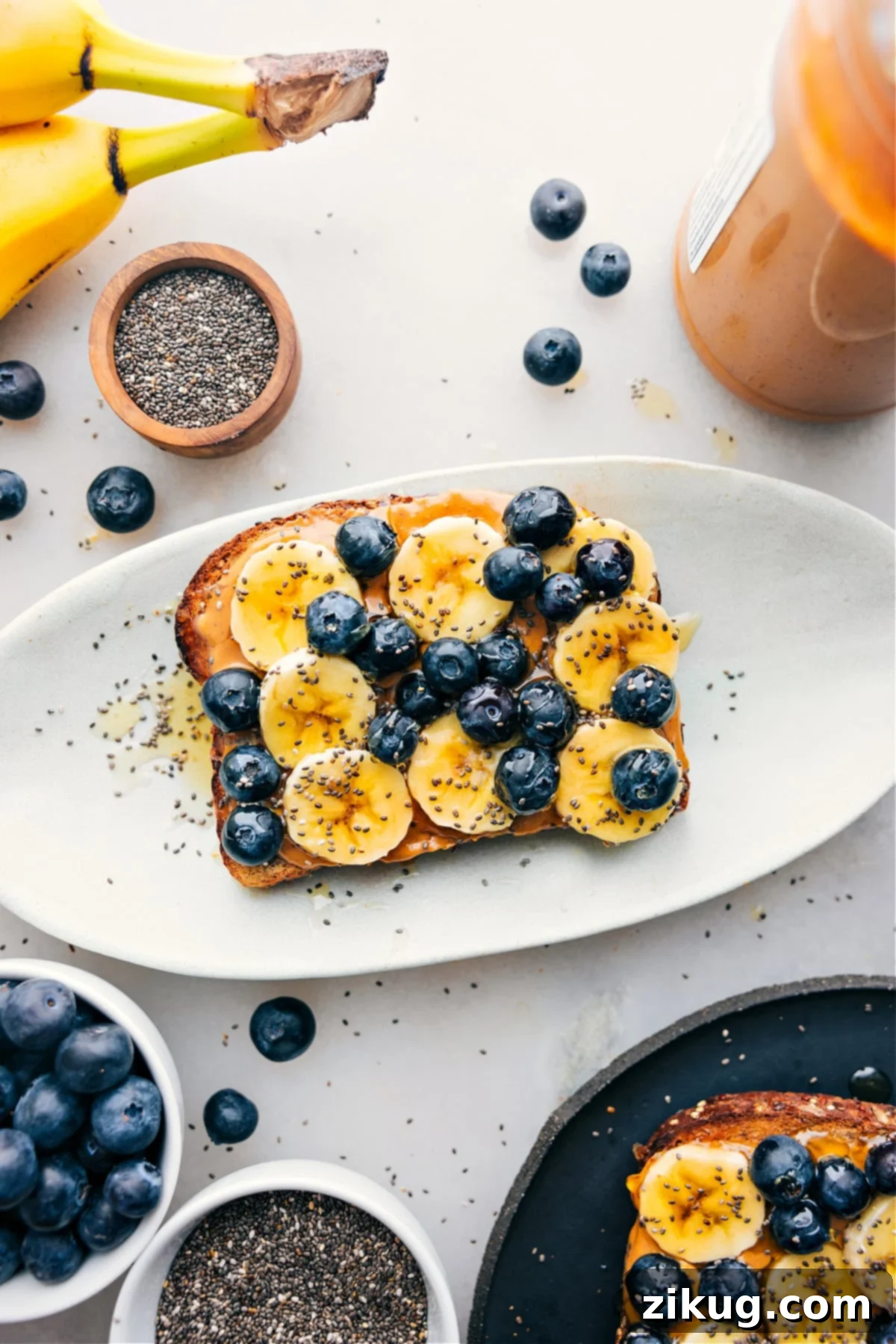 A beautifully arranged breakfast toast on a platter, showcasing a vibrant array of toppings including banana slices, fresh blueberries, a sprinkle of chia seeds, and a glistening drizzle of honey.