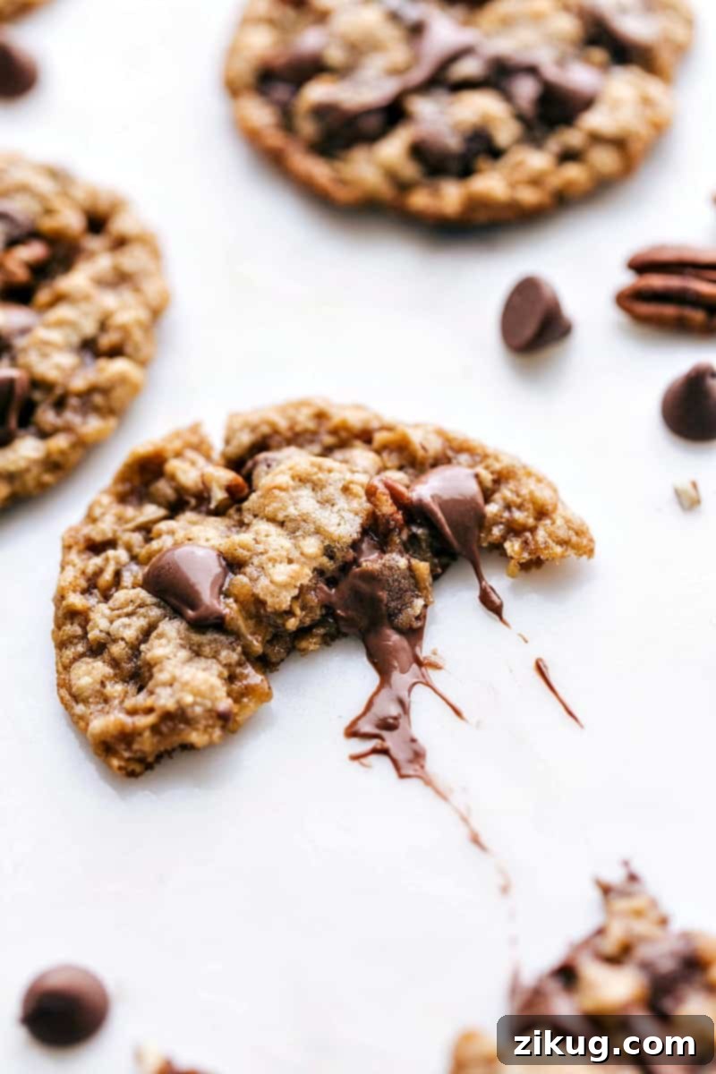 A close-up of a freshly baked oatmeal chocolate chip pecan cookie, split in half to showcase its gooey, melted chocolate center and tender crumb.