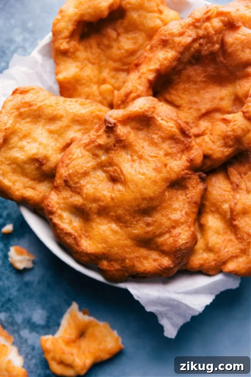 Homemade Fry Bread is a flatbread made with simple and accessible everyday ingredients. The dough is deep fried in oil and can be enjoyed right out of the oil or with various toppings -- sweet or savory. This easy recipe from Chelsea's Messy Apron creates the best crispy and chewy results. #fried #best #quick #easy #simple #carnival #fry #bread #frybread Overhead image of freshly made Fry Bread on a plate, ready to be served with various toppings.