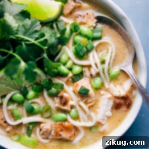 A vibrant bowl of Green Curry Noodle Soup with chicken and edamame, garnished with fresh herbs.