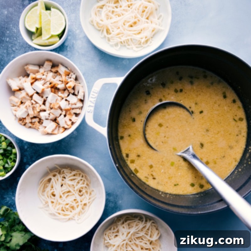Close-up of bowls being prepped with ingredients before adding the rich Green Curry Noodle Soup broth, showing fresh lime wedges and cilantro as serving suggestions.