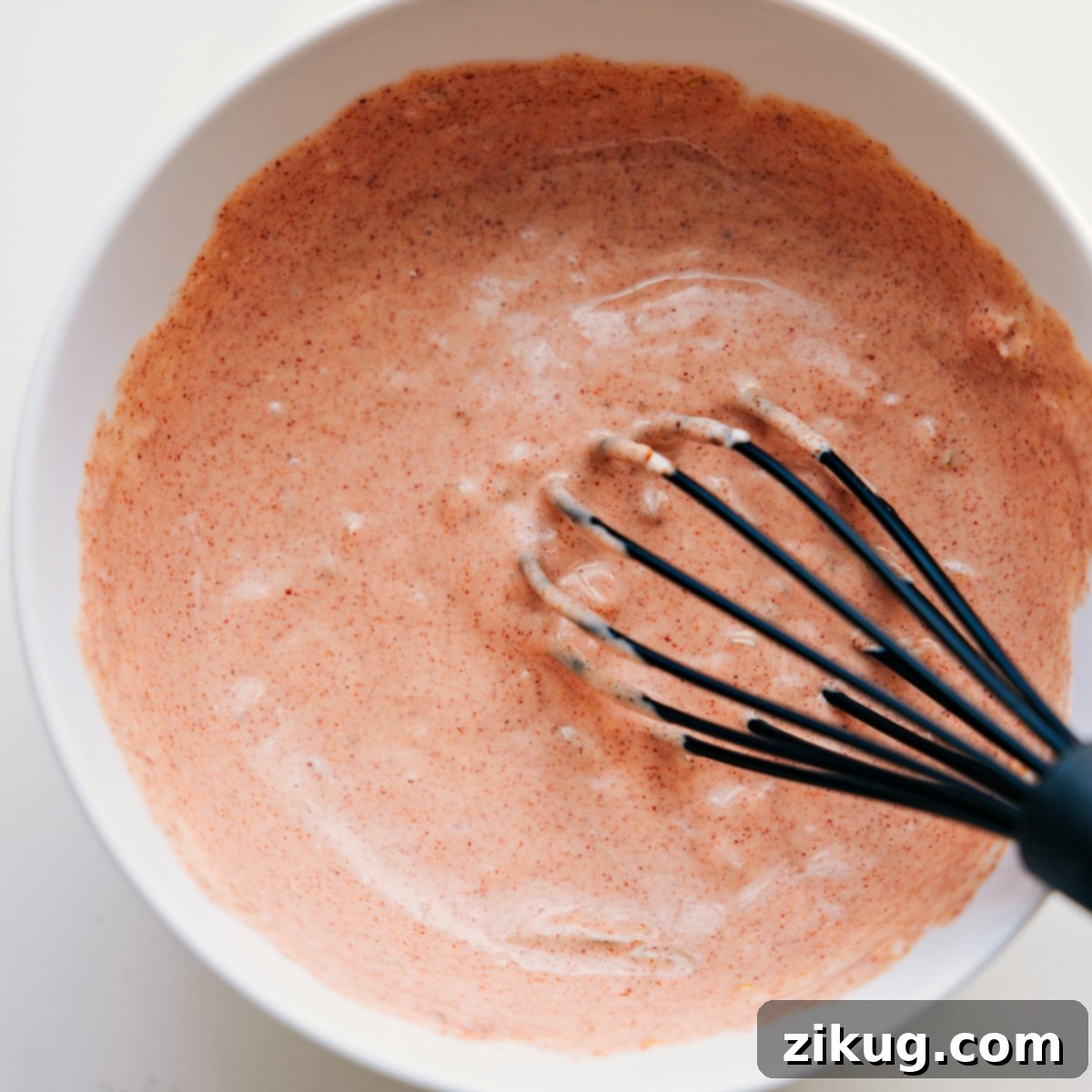The delicious homemade burger sauce being whisked in a glass bowl, showcasing its creamy texture, ready to be drizzled over the burger bowls.