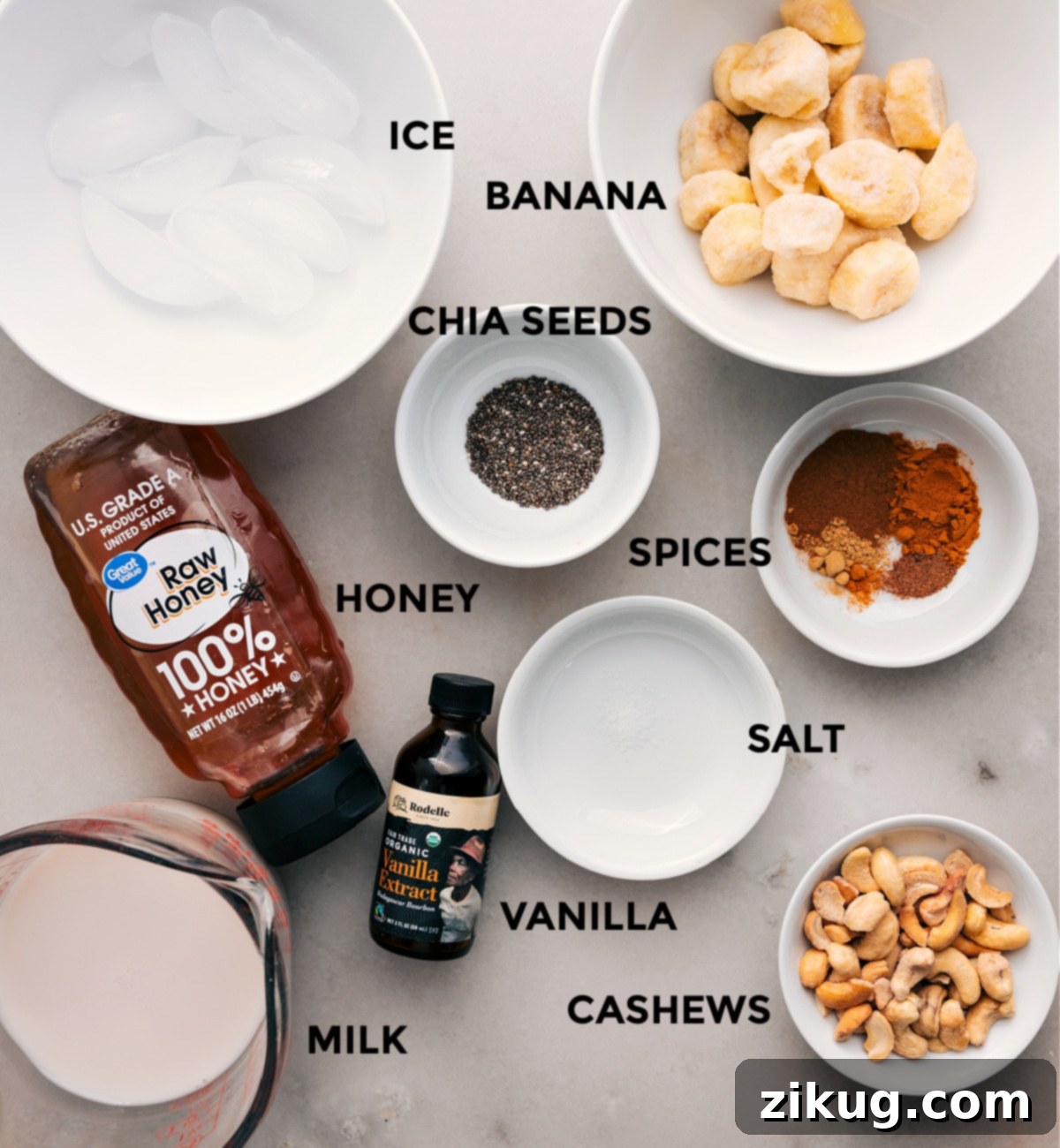 Essential Ingredients for Your Golden Milk Smoothie A beautifully arranged spread of ingredients for a Golden Milk Smoothie: whole cashews, various spices in small bowls, a golden drizzle of honey, vanilla extract, a pinch of salt, milk, and sliced frozen bananas ready for blending.