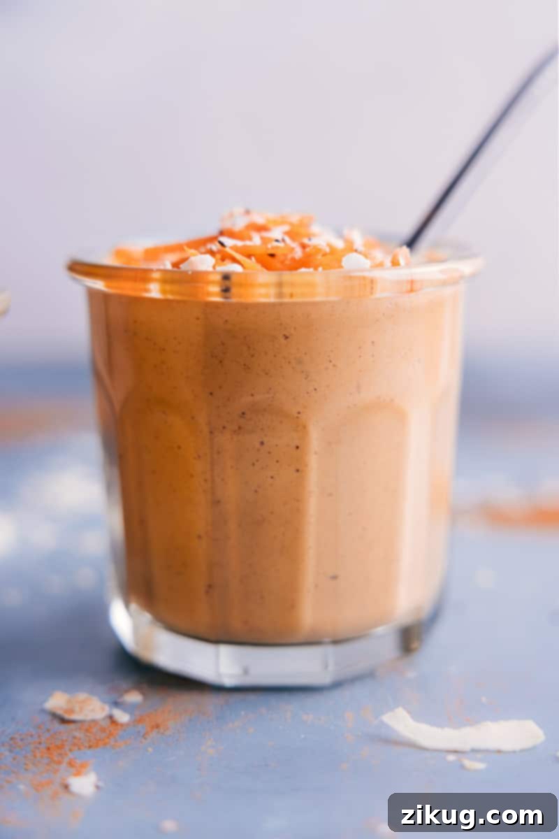 Our favorite Carrot Smoothie is the perfect way to channel your cravings for Carrot Cake without having to bake anything. This protein-packed, nutritious, and filling smoothie is healthful, but somehow tastes almost as indulgent as a cake! Recipe via ChelseasMessyApron #quick #easy #simple #snack #best #healthy #fresh #cleaneating #wholefoods #carrot #smoothie A simple, elegant shot of a Carrot Smoothie in a clear glass with a reusable straw, ready to be enjoyed. The focus is on the rich, creamy texture and inviting color of the drink.