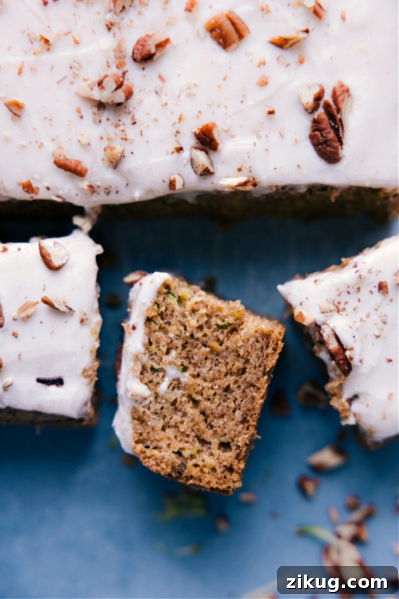 Image of the Healthy Zucchini Cake on a serving platter, with a slice removed to show its moist interior and thick layer of cream cheese frosting.