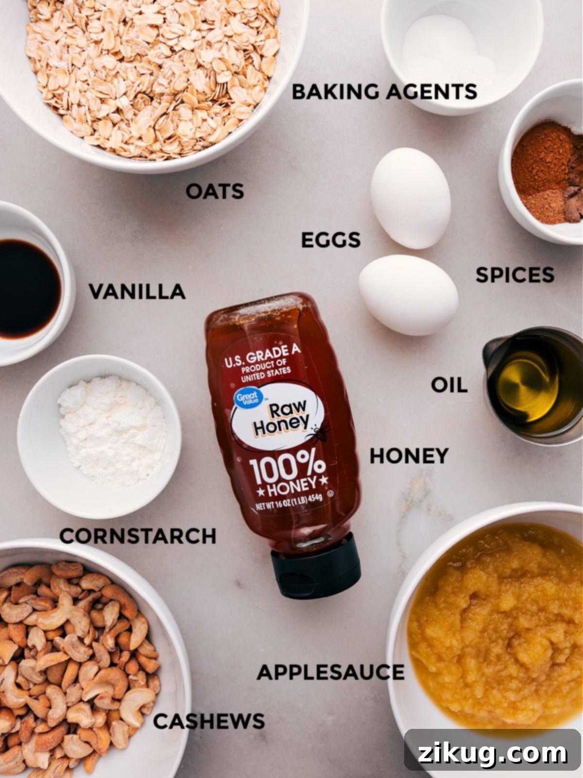 Prep all the ingredients for this recipe, including oats, baking agents, eggs, spices, oil, honey, vanilla, cornstarch, cashews, and applesauce, for easy assembly.