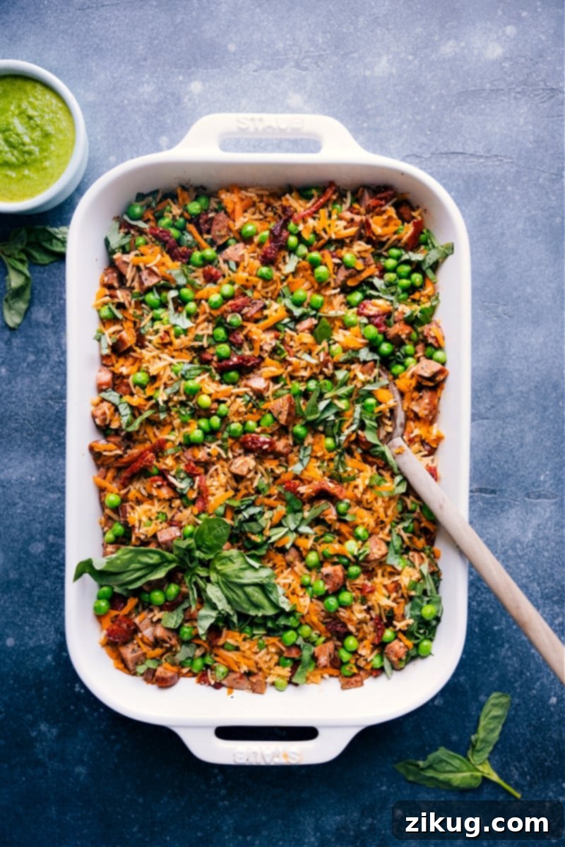 Overhead view of a vibrant One-Pan Pesto Rice dish, showcasing tender rice, smoked chicken sausage, and various vegetables, garnished with fresh basil.